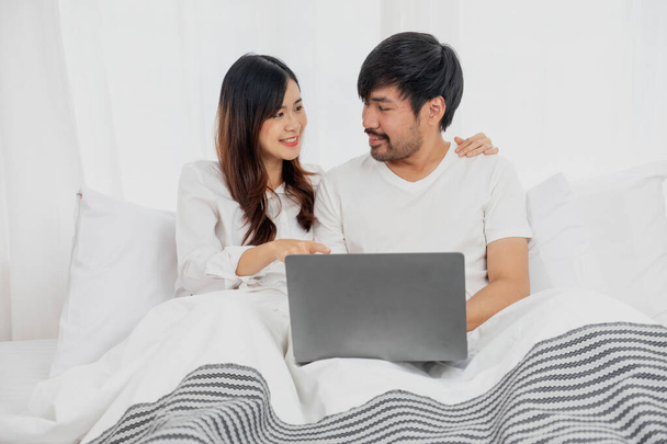 Joven pareja asiática feliz usando el ordenador portátil en la cama viendo la película, tiempo romántico para mejorar la relación familiar, concepto de familia. - Foto, imagen