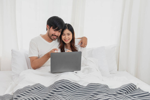 Jeune couple asiatique heureux à l'aide d'un ordinateur portable au lit regarder film, temps romantique pour améliorer la relation familiale, concept de famille. - Photo, image