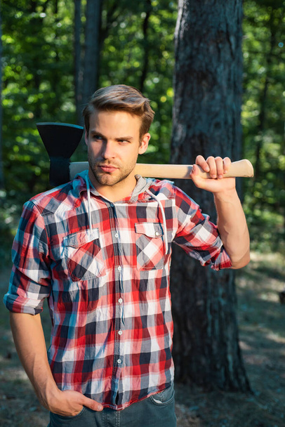 Stylish young man posing like lumberjack. The Lumberjack working in a forest. Handsome man with axe. Strong man lumberjack with an ax in a plaid shirt - Fotografie, Obrázek