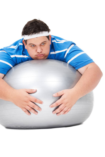Tired, plus size and man on exercise ball feeling fatigue from training and workout in studio. Lazy, thinking and rest of a male person doing weight loss and wellness practise on gym equipment. - 写真・画像
