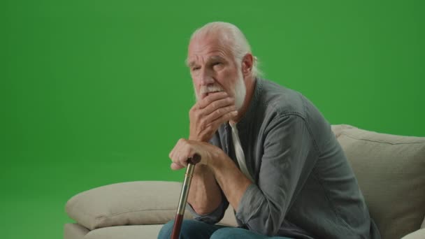 緑の画面。棒を持つ悲しい老人の肖像画はソファに座っています.高齢の男は棒で頭を傾け、灰色のひげをこすります.高齢者のための精神衛生. - 映像、動画