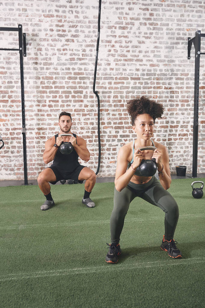 Discipline is the one thing needed to achieve any goal. two people holding kettlebells while doing squats at the gym - Zdjęcie, obraz