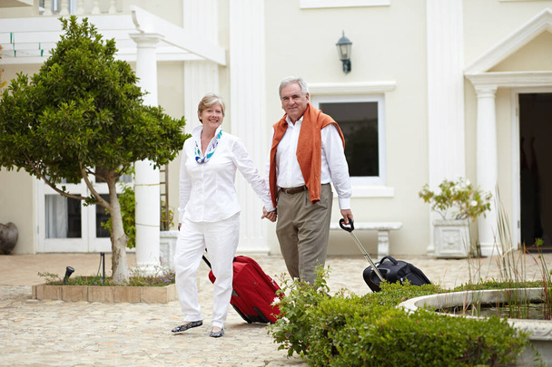Ταξίδι, ξενοδοχείο και ευτυχισμένο ζευγάρι ηλικιωμένων περπάτημα με βαλίτσα σε μια τοποθεσία διακοπών ή διακοπών στη συνταξιοδότηση μαζί. Τσάντα, χαμόγελο και ηλικιωμένοι σε ένα ταξίδι ή άντρας και γυναίκα περπατούν στην ευτυχία. - Φωτογραφία, εικόνα