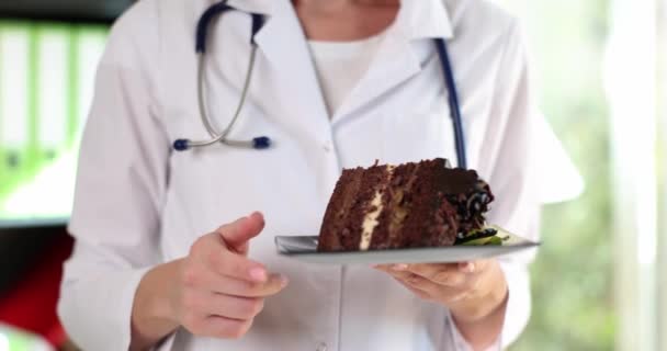 Nutritionist doctor holds piece of cake and warns about dangers of sweets. Sugar benefits and harms to human health - 映像、動画
