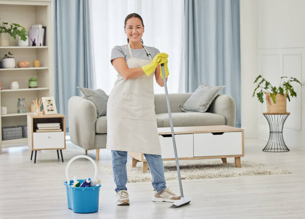 Retrato, vassoura e uma mulher limpadora varrendo a sala de estar de uma casa para higiene, serviço ou tarefas domésticas. Sorriso, limpeza de primavera ou limpeza com uma empregada feminina asiática em pé em uma casa doméstica. - Foto, Imagem