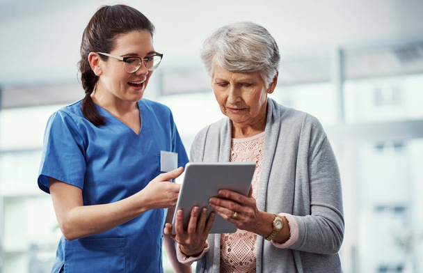 Jetez un oeil ici... une jeune infirmière et sa patiente âgée regardant une tablette dans la maison de retraite - Photo, image