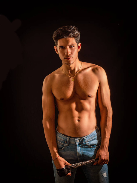 Handsome muscular shirtless young man standing confident, looking at camera on black background - Фото, изображение