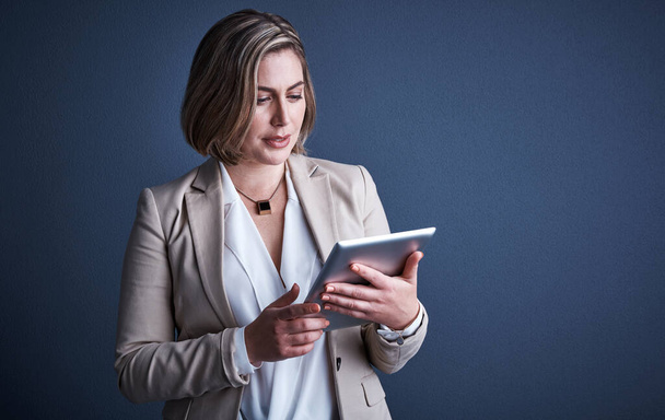Using technology to her benefit. Studio shot of an attractive young corporate businesswoman using a tablet against a dark background - Foto, Bild