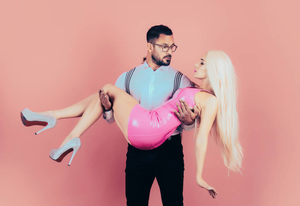 Handsome elegant young man holding his girlfriend in his arms. Funny Valentines day. Fun couple on pink isolated background. Funny man holds and hug woman in arms. Sexy couple - Foto, Imagem