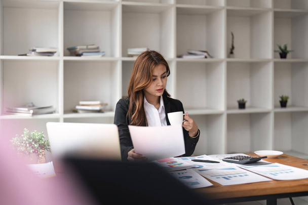 Vážná mladá asijská podnikatelka pracující s finanční papírování sedí v kanceláři. - Fotografie, Obrázek