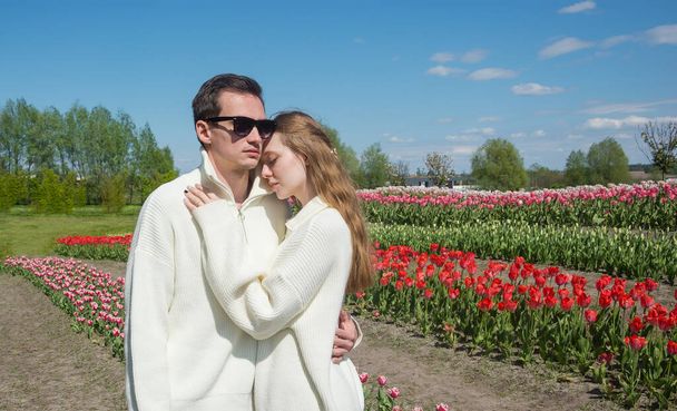 Jovem lindo casal sorridente no fundo de um campo de tulipas coloridas. Guy e menina abraço togather - Foto, Imagem