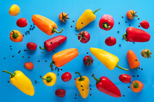 Falling bell pepper and tomatos on blue background. Flying colorful sweet peppers. Banner. Vegetable pattern for packaging design. Healthy food. - Fotó, kép