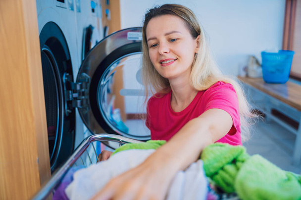 Young beautiful woman washes and dries clothes in the laundry. - Valokuva, kuva