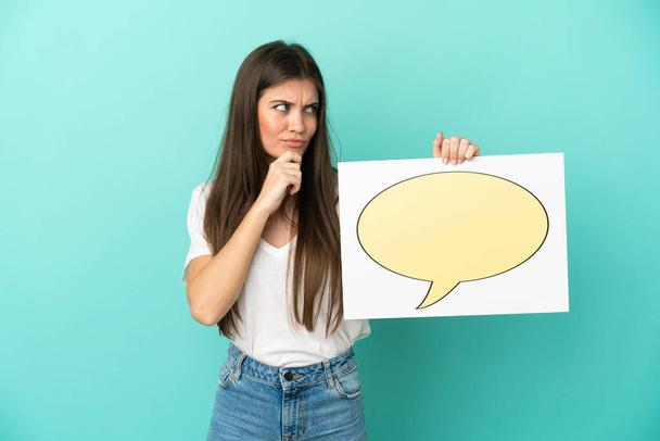 Young caucasian woman isolated on blue background holding a placard with speech bubble icon and thinking - Fotó, kép