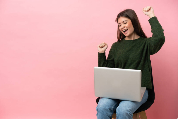 Young caucasian woman sitting on a chair with her laptop isolated on pink background celebrating a victory - Foto, imagen