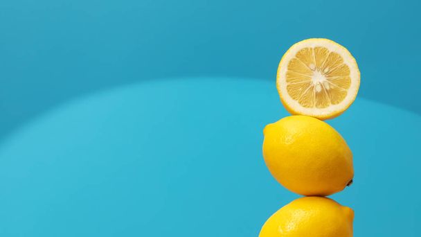 A pyramid of juicy yellow lemons on a blue background. Creative concept of fruits, citrus fruits. Healthy eating. Copy space - Photo, image