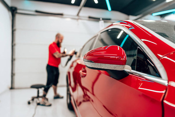 Professional vehicle polishing and detailing service in a modern car workshop. Brightly lit workspace with large led lights. High quality car valeting concept. - Photo, Image