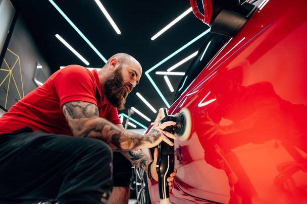 Professional vehicle polishing and detailing service in a modern car workshop. Brightly lit workspace with large led lights. High quality car valeting concept. - Foto, Bild