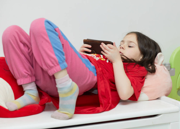 молода дівчина грає на мобільному телефоні, перебуваючи в її кімнаті
 - Фото, зображення