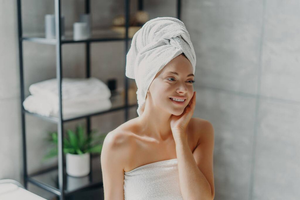Smiling spa lady with natural makeup poses refreshed after shower, touches healthy skin in bathroom. - Fotografie, Obrázek