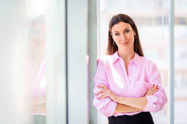 Portrait shot of an attractive businesswoman looking at camera and smiling while standing with arms crossed in a modern office. - Φωτογραφία, εικόνα