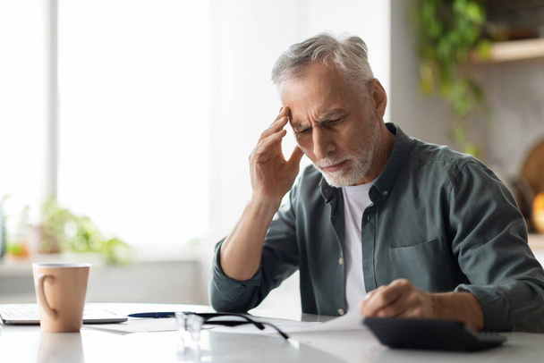 Stressed Senior Man Checking Papers While Sitting At Desk In Kitchen At Home, Frustrated Elderly Gentleman Reading Bills Or Tax Form, Having Problem With Bank Documentation, Copy Space - Foto, imagen