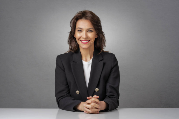 Attractive brunette haired businesswoman wearing blazer and sitting at isolated background. Copy space. - Foto, Imagem