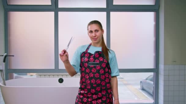 portrét mladé usměvavé ženichovy dívky v zástěře s profesionálními nůžkami v rukou zvířecí péče v domácím salonu - Záběry, video