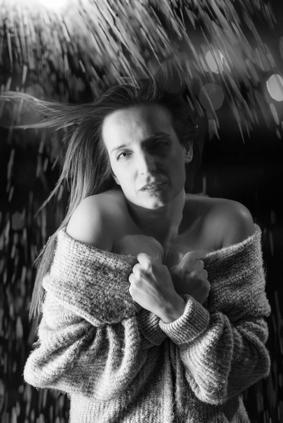 fekete-fehér portré egy fiatal nőről, aki fázik, miközben a pulcsiját fogja egy elveszett gondolattal. - Fotó, kép