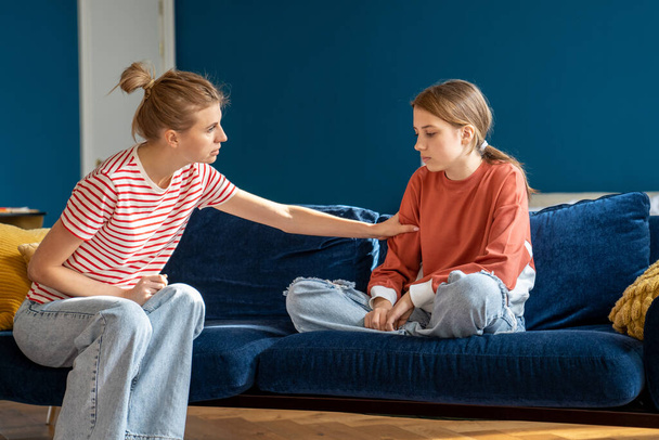 Young woman loving mother trying to speak with upset depressed teen daughter while sitting together on sofa at home, mom comforting teenage girl child, showing support. Anger in adolescents - Foto, imagen