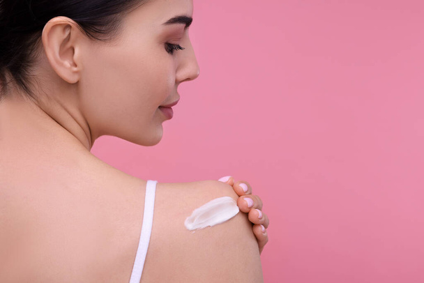 Beautiful woman with smear of body cream on her shoulder against pink background, back view. Space for text - Fotoğraf, Görsel