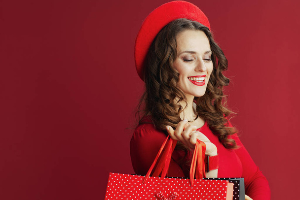 Happy Valentine. smiling stylish woman in red dress and beret with shopping bags isolated on red. - Fotó, kép