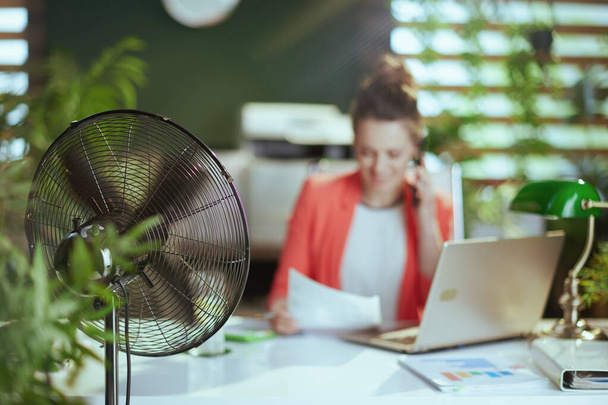 Sustainable workplace. Closeup on happy modern woman worker at work with electric fan and laptop. - Фото, зображення