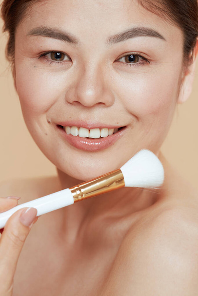 Portrait of modern woman with makeup brush on beige background. - Zdjęcie, obraz