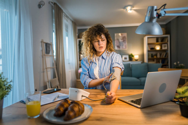 Egy kaukázusi nő szabadúszó ül az asztalnál munka közben ellenőrizze a vérnyomást otthon valós személy egészségügyi koncepció - Fotó, kép