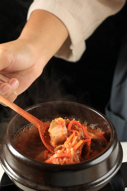 Kobieca ręka gotowania zupa Kimchi Gulasz lub Kimchi Jigae, Koreański Tradycyjne jedzenie wykonane ze sfermentowanej kapusty Nappa, Gochujang, Czosnek, i warzyw - Zdjęcie, obraz