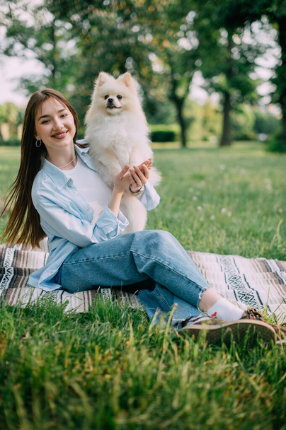 Young woman with her cute dog in park. Pomeranian Spitz with his owner are sitting on the grass. - Foto, imagen