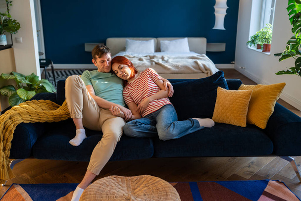 Couple amoureux assis sur le canapé et tenir la main, embrassant dans son propre appartement. L'homme et la femme se lient, profitant d'un moment ensemble à la maison. Lien émotionnel dans la relation - Photo, image