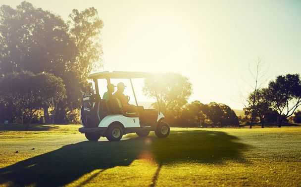 Getting into the swing of things. two golfers riding in a cart on a golf course - Foto, imagen