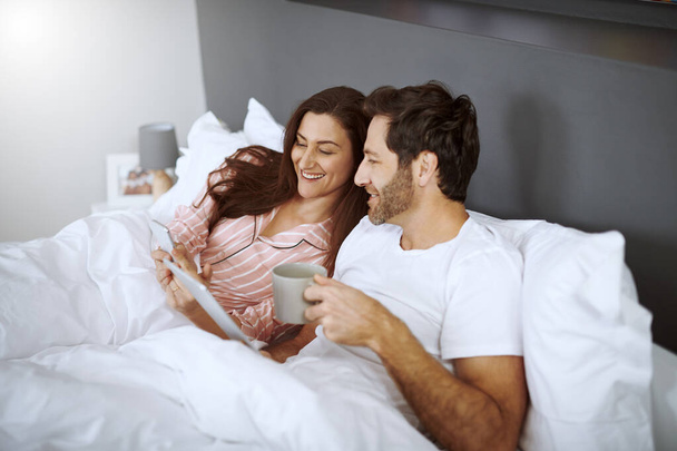 Mira este post. una pareja usando sus dispositivos inalámbricos mientras están acostados en la cama - Foto, Imagen