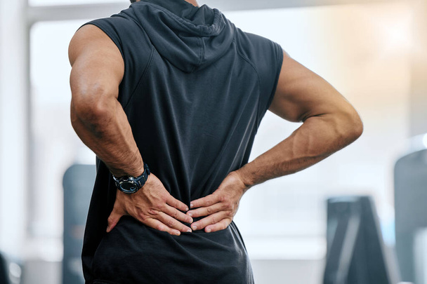 Gym, injury and man with hand on back pain for medical emergency from workout at sports studio. Exercise, health and wellness, bodybuilder with hands on muscle to massage ache or cramp while training. - Photo, Image