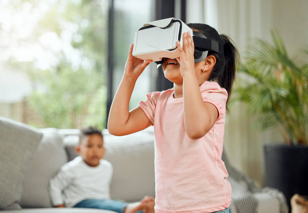 Young girl with VR goggles, gaming and metaverse with futuristic tech, child experience simulation at family home. Female kid in living room with video games, virtual reality and future technology. - Fotó, kép