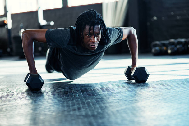 Napról napra erősebb lesz. Egy fiatal férfi fekvőtámaszozik súlyzókkal az edzőteremben. - Fotó, kép