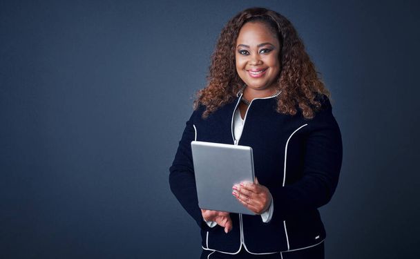 She has all of your answers. Portrait of a confident young businesswoman working on her digital tablet while standing against a blue background - Photo, Image