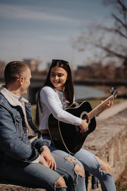 Lähikuva kaunis brunette tyttö pelaa kitaraa hänen poikaystävänsä istuessaan - Valokuva, kuva