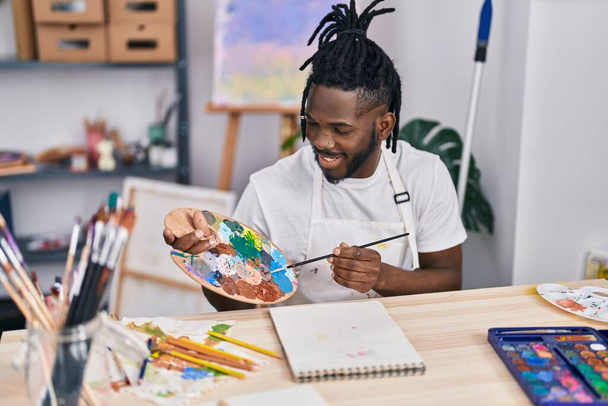 Afrikaans amerikaanse vrouw glimlachen zelfverzekerd tekenen op notebook in kunst studio - Foto, afbeelding