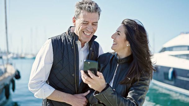 Мужчина и женщина улыбаются уверенно, используя смартфон в порту - Фото, изображение