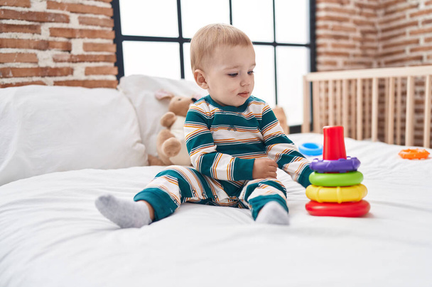Αξιολάτρευτο καυκάσιος μωρό παίζει με στεφάνες κάθεται στο κρεβάτι στο υπνοδωμάτιο - Φωτογραφία, εικόνα