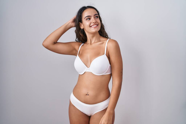 Young hispanic woman wearing white lingerie smiling confident touching hair with hand up gesture, posing attractive and fashionable  - Φωτογραφία, εικόνα