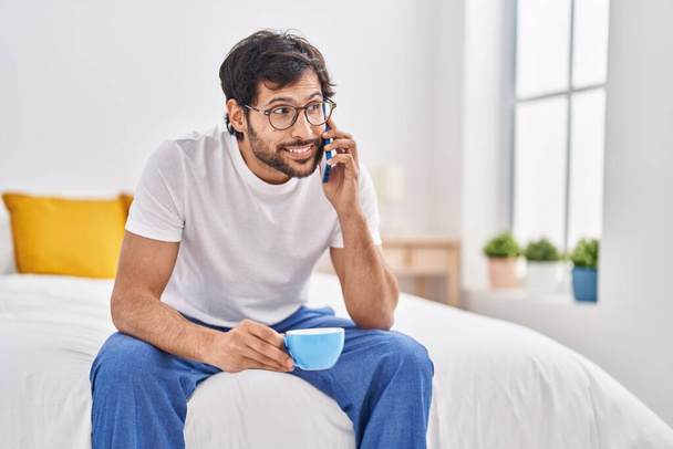 Jeune homme hispanique parlant sur le smartphone boire une tasse de café dans la chambre - Photo, image